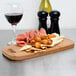 An American Metalcraft carbonized bamboo serving board with food and a glass of wine on it.