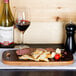 An American Metalcraft carbonized bamboo serving board with a plate of crackers, meat, and a glass of wine on a table.