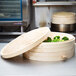 A Town bamboo steamer cover on a stack of round wooden baskets with food inside.