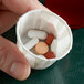 A hand holding a Genpak paper souffle cup filled with pills.