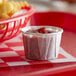 A small paper cup of ketchup in a red basket with french fries.