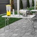 A Regency stainless steel folding work table on a patio with a drink dispenser and a blender.