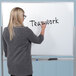 A woman writing "teamwork" on a Luxor magnetic glass whiteboard.