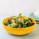 A yellow Fiesta china bistro bowl filled with salad on a table.