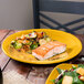 A close up of a piece of salmon and vegetables on a yellow Fiesta® chop plate.