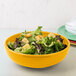 A yellow Fiesta china bistro bowl filled with salad on a table.