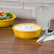A yellow Fiesta china bowl with white liquid and a bowl of salad on a table.