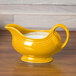 A yellow Fiesta gravy boat with a white handle on a wood surface.