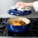 A woman using a towel to put food in a Lodge indigo enameled cast iron Dutch oven.
