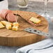 An American Metalcraft bamboo round cutting board with cheese and meat on it, with a knife.