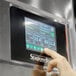 A hand touching a screen with a digital display on a Stagionello meat curing cabinet.