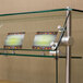 An Advance Tabco glass sneeze guard on a counter with signs on glass shelves.