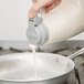 A person pouring milk from a Tablecraft dispenser into a pan.