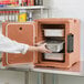 A woman in a white coat opening a Cambro Ultra Pan Carrier in a professional kitchen.