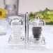 A clear salt and pepper shaker set on a table with a white tablecloth.