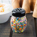 A Tablecraft black plastic slotted shaker top filled with sprinkles on a table.