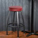 A Lancaster Table & Seating black bar stool with a red cushion.