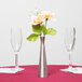 A Tablecraft metal hourglass bud vase with flowers on a table with two empty wine glasses.