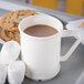 A close up of a white Carlisle polycarbonate mug filled with hot chocolate and marshmallows on a tray with cookies.