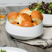 A 10 Strawberry Street Arctic Blue porcelain bowl filled with bread rolls on a table with a salad.