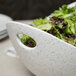 A 10 Strawberry Street blue speckled porcelain bowl with cut-out handles filled with green lettuce on a table.