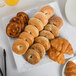 A 10 Strawberry Street blue speckled square porcelain platter with bagels, croissants, and orange juice on it.