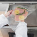 A person's hand holding a VacPak-It chamber vacuum bag filled with chicken with lemon slices.