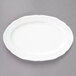 A Tuxton Charleston bright white china oval platter with a scalloped edge on a gray surface.