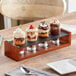 An Acopa wooden tray with Barbary tasting glasses holding a row of desserts.