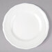 A Tuxton TuxTrendz Charleston white china bread and butter plate with scalloped edges on a gray surface.
