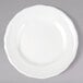 A Tuxton TuxTrendz Charleston white china bread and butter plate with scalloped edges on a gray surface.