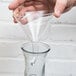 A hand using a Franmara glass decanter funnel to pour liquid into a glass.