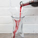 A person using a Franmara glass decanter funnel to pour red wine into a glass.