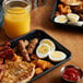 A breakfast platter with hard cooked eggs, bacon, sausage, and hash browns on a table with orange juice.
