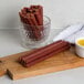 A wooden cutting board with Weaver's hot beef sticks, mustard, and a glass of liquid.