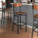 Three Lancaster Table & Seating Boomerang Series Black Finish Bar Stools with Antique Walnut Wood Seats and Backs at a kitchen counter.