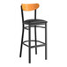 A black bar stool with a black vinyl seat and cherry wood back.