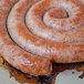 A Fontanini Moda Nostra sweet Italian sausage rope cooked in a spiral on a pan.