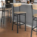 Three Lancaster Table & Seating Boomerang black bar stools with driftwood seats at a wooden table in a bar.