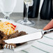 A hand holding a Oneida steak knife and fork over a plate of food.