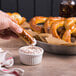 A hand dipping a Dutch Country Foods soft pretzel into a bowl of dip.