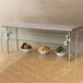 A stainless steel counter shelf with an Advance Tabco Sleek Shields food shield on it over bowls of fruit.
