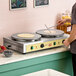 A dual steel crepe maker with two large round cooking surfaces and control knobs, designed for commercial use.