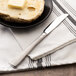 A Oneida stainless steel butter knife on a plate of bread with a piece of butter.