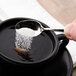 A Oneida Perimeter stainless steel demitasse spoon scooping sugar into a cup of liquid.