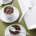 A Oneida Libra stainless steel cocktail fork with coffee beans in a white cup with a spoon.