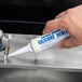 A hand holding a white tube of FMP Clear Silicone Plumber's Sealant with blue text.
