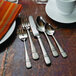 A close-up of a Oneida Satin Astragal stainless steel round bowl soup spoon on a table set with other silverware.