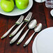 A table with a plate of green apples and a Oneida Sestina stainless steel dinner fork on it.
