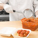 A person uses a Vollrath Black Perforated Spoodle to strain meatballs from a container of pasta.